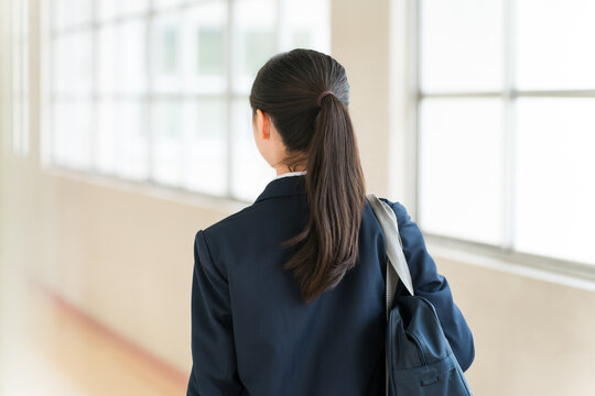 The backs of elementary, middle, and high school girls in school uniforms walking down a school corridor.
