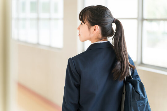 The backs of elementary, middle, and high school girls in school uniforms walking down a school corridor.