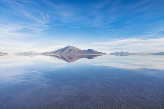 Vast salt flat reflecting mountains and sky.