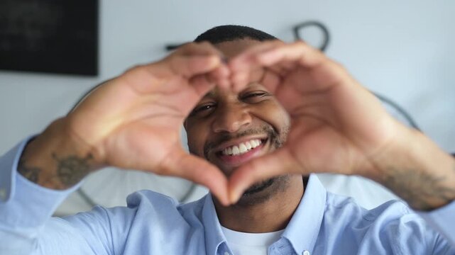 Happy smiling man showing love sign with his hands looking at camera in a modern apartment