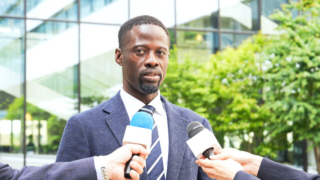 A Black man being interviewed while surrounded by a group of reporters.