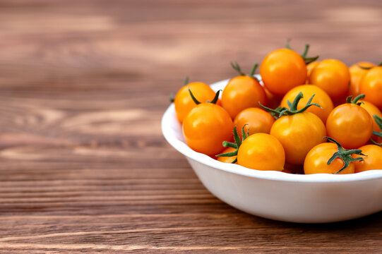 Full white ceramic bowl of bright orange cherry tomatoes, Sungold variety, on the brown rustic wooden table.