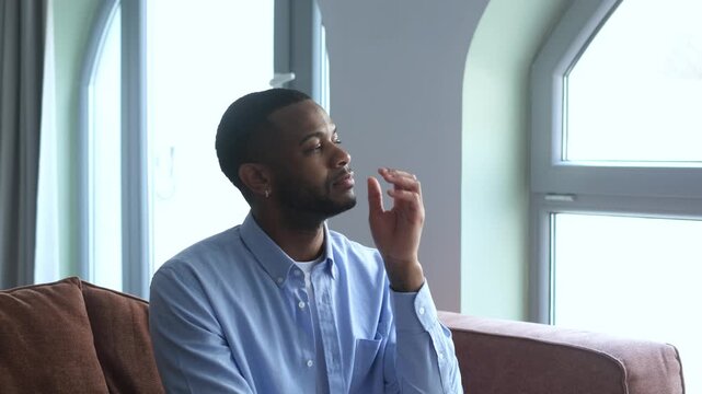 Thoughtful young man sitting on a sofa and looking out the window, feeling calm and dreaming