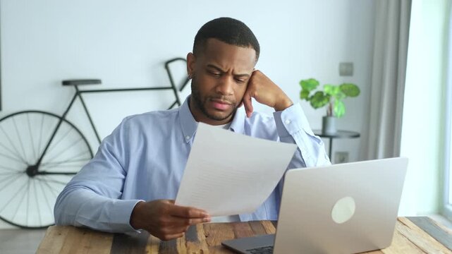 Frustrated young man feeling stressed while reading a financial report or a letter at his desk