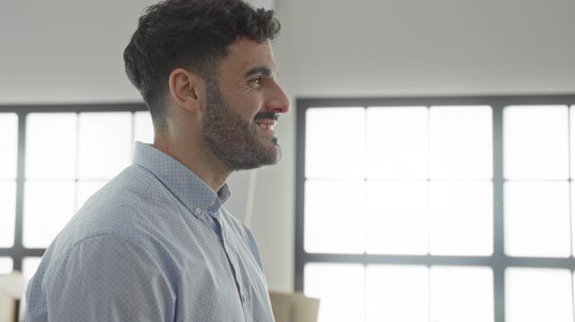 Man smiling with face in profile, looking at moving boxes near bright windows in building; optimism fresh start.