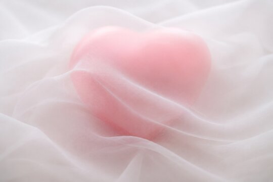 A soft pink heart shape veiled by translucent white chiffon fabric with delicate folds.