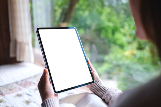 Mockup image of a woman holding tablet with blank desktop white screen on the bed at home