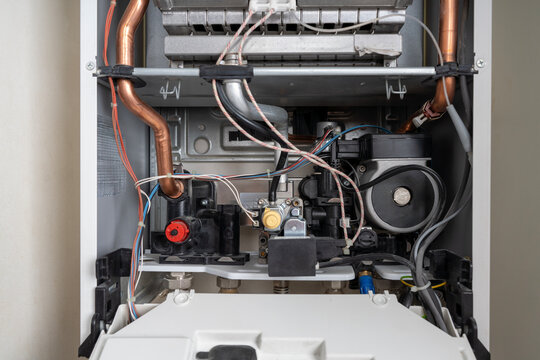 Close-up of lower internal components of an open domestic gas boiler, showing circulation pump, gas valve, copper pipes, and electrical wiring during service.