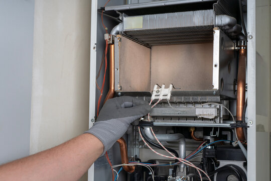 Technician hand in a protective glove inspecting the ignition electrode wiring inside the open combustion chamber of a domestic gas boiler during maintenance.