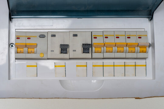 Close-up of a domestic electrical consumer unit panel filled with automatic circuit breakers and fuse switches under an open plastic cover.