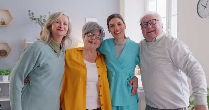 Happy cheerful senior people enjoying time in the retirement home. Smiling joyful old men and women together with a young friendly nurse girl posing for a group photo together