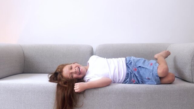 Happy little girl having fun lying on couch at home - Focus on child face 