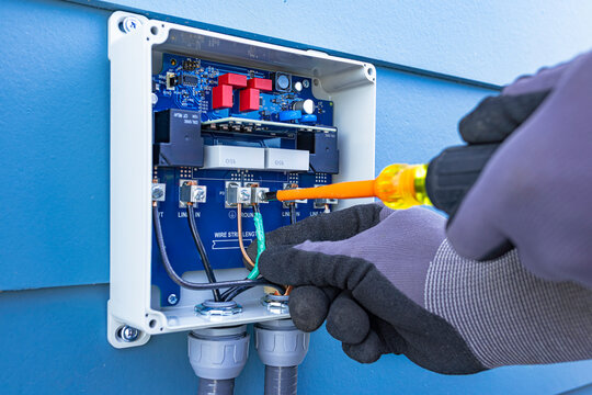 Close up view of electrician hands using an insulated screwdriver to wire an outdoor surge protector for an HVAC air conditioner unit