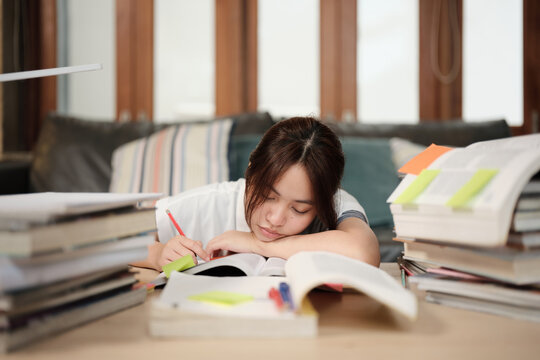 College Asian teenage girl tired and burned out from overwhelmed study pile of books, stressed learning at home with stack of textbooks, reading and writing for school exam, homeschooling education.