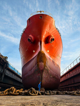 A shipyard worker stands proudly in front of a giant cargo ship under maintenance in a dry dock.