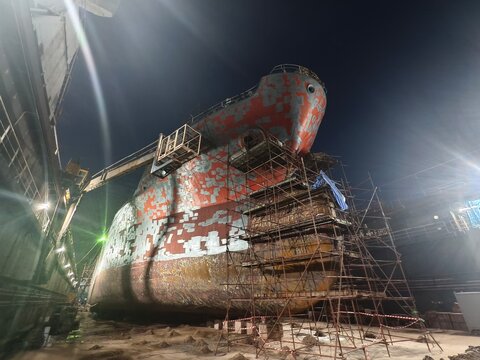 Large cargo ship under intensive maintenance in a dry dock at night.