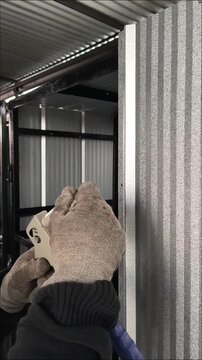 Worker hands loading and using a hand rivet gun on a corrugated metal storage unit