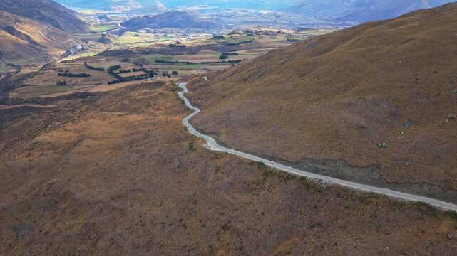 Winding mountain road ascends through dry alpine landscape with valley views below