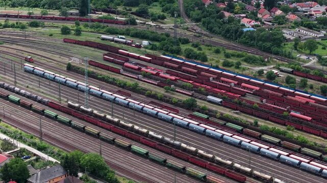 An aerial view captures multiple freight trains parked on parallel tracks at a busy logistics rail yard in rural Hungary.