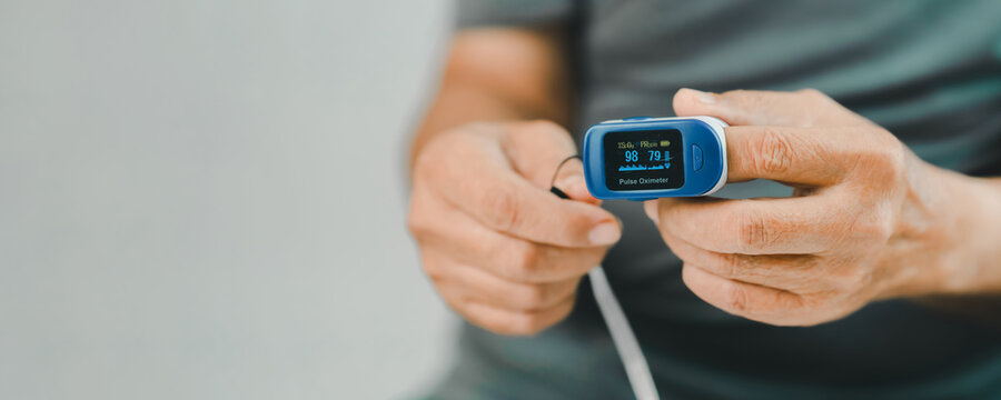 Close-up of a senior adult using a fingertip pulse oximeter to measure blood oxygen saturation and pulse rate at home. Home health monitoring supports preventive care, chronic disease management