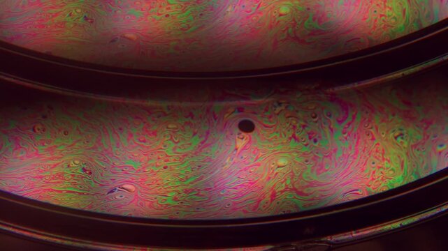 Iridescent fuel. Paint mix. Defocused pink purple green colorful round oil texture chemical drop liquid spill on abstract dark black background.
