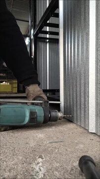 Close up of a worker drilling a hole in a metal sheet structure at ground level