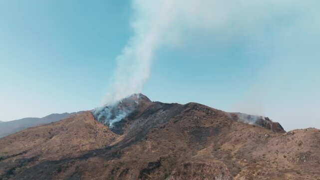 Mountainside after a forest fire with smoke billowing from smoldering vegetation in Mexico
