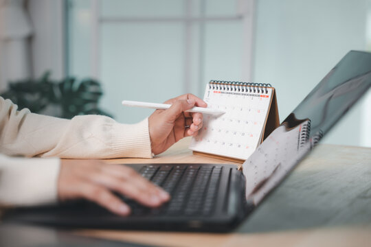 Person using pen for calendar planning to circle event time, scheduling business meeting and medical checkup appointment while writing schedule on desk laptop computer during workday