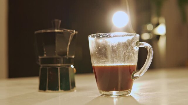 Steaming hot coffee in a glass cup with italian moka pot