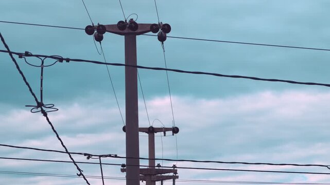 Multiple concrete utility poles and power lines against a cloudy blue sky