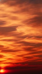 Fototapeta premium Intense orange and red sunset sky with swirling, wispy cloud formations creating a fiery and dramatic atmosphere as the sun dips below the horizon, casting a warm glow across the wallpaper background