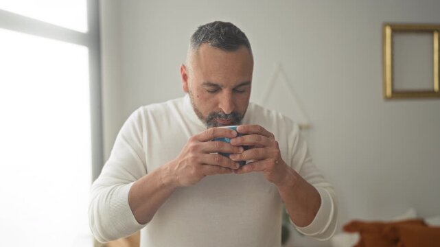 Man holding a mug with both hands, eyes closed while savoring coffee in a building; morning ritual contentment.