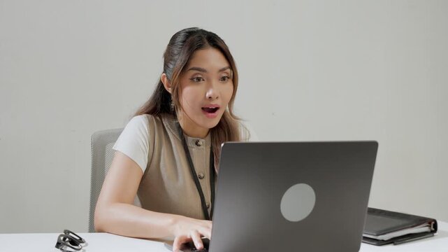 Beautiful young Asian woman is typing report on her laptop while feeling happy.