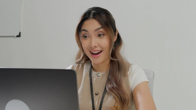 Beautiful young Asian woman is typing report on her laptop while feeling happy.