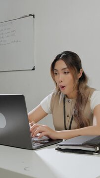 Beautiful young Asian woman is typing report on her laptop while feeling happy.