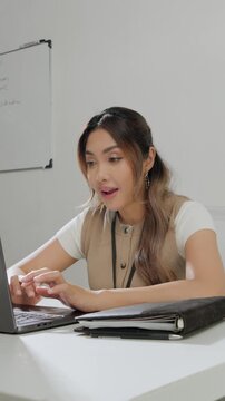 Beautiful young Asian woman is typing report on her laptop while feeling happy.