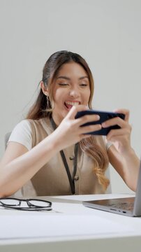 Joyful young Asian woman is watching streaming video or playing game on her smartphone.