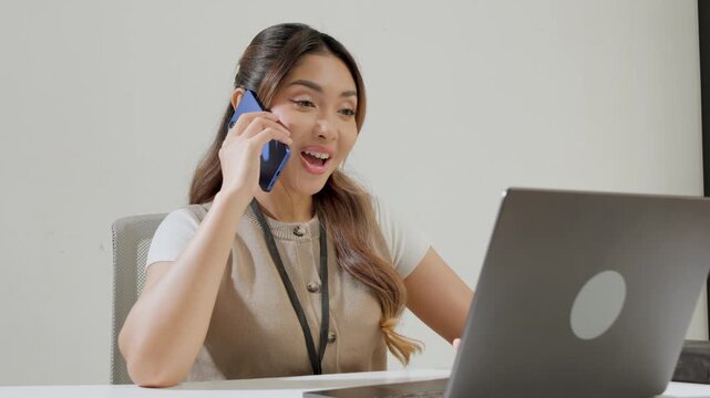Smiling young Asian business woman is working while using smartphone and having a call for meeting.