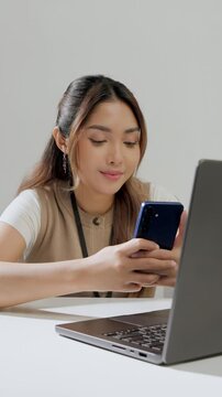 Cheerful young Asian woman is working while using smartphone to text someone or open social media.