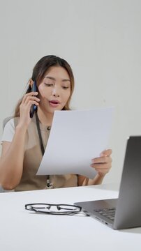 Smiling young Asian business woman is working while using smartphone and having a call for meeting.