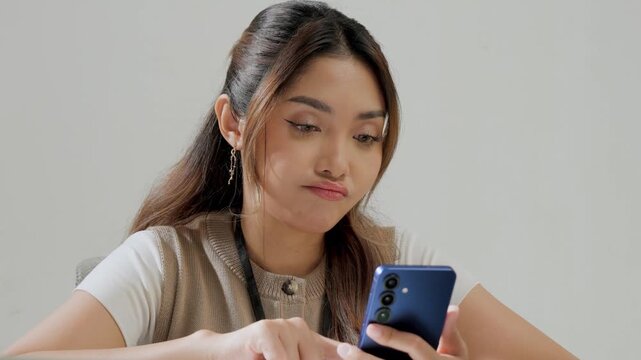 Happy young Asian woman is working while using smartphone to text someone or open social media.