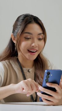 Happy young Asian woman is working while using smartphone to text someone or open social media.