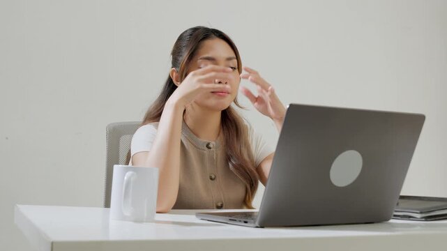 Young Asian female employee is working using her laptop while feeling headache and stressful.