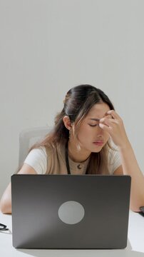 Young Asian female employee is working using her laptop while feeling headache and stressful.