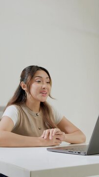 Serious young Asian business woman sitting down with a laptop while having discussion meeting.