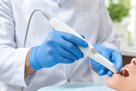 Professional dentist in white coat and blue gloves performing dental examination with digital scanner on patient teeth in modern clinic, healthcare concept