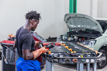 Professional EV technician using a diagnostic scanner to inspect a high-voltage battery pack in a modern electric vehicle workshop. © kamonrat