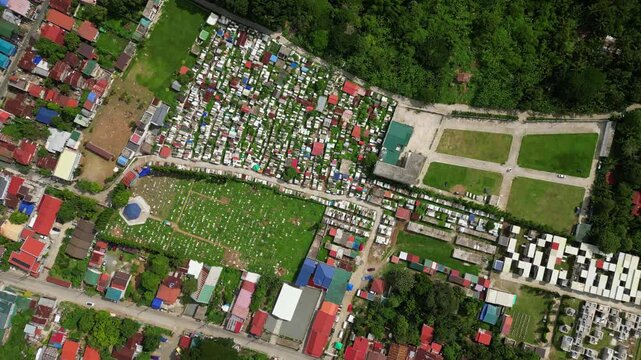 Slow pan drone footage across Alfonso Public Cemetery in Cavite Philippines featuring rows of tombs, pathways, and the surrounding town environment in daylight.