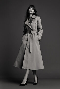 Woman in Long Trench Coat Standing in Dark Minimalist Setting with Elegant Style