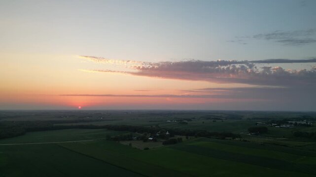 Pulling back flying high in a drone above an Iowa sunset farm field with a cloud bank rolling in. An evening so hot humidity in the air starting to take shape on the horizon as fog. Drone, 4k, flying